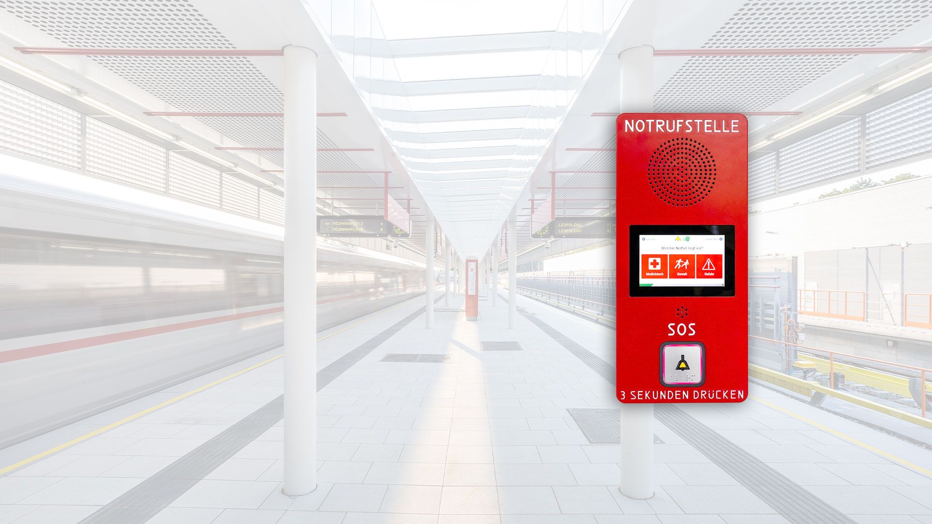 Rotes Notrufgerät mit Lautsprecher, Bildschirm und SOS-Knopf in einem hellen Bahnhofsgebäude