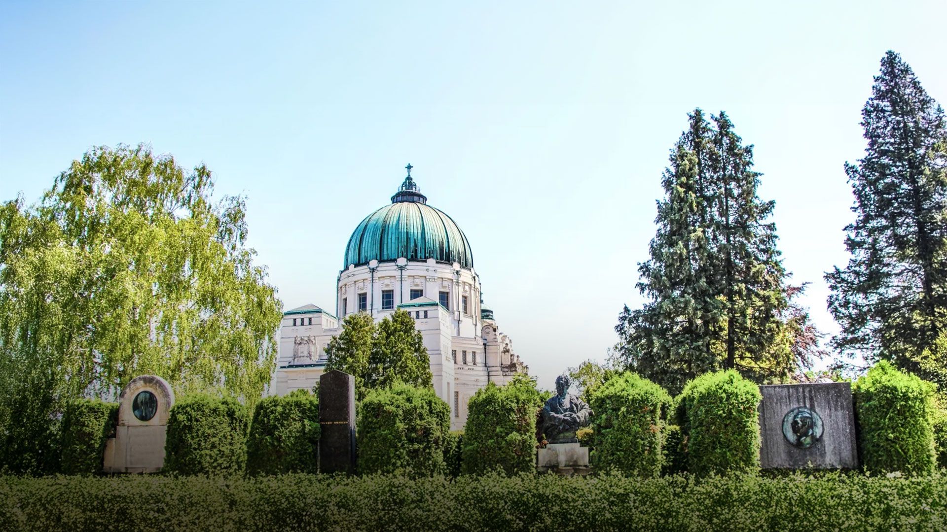 Historisches Mausoleum mit grünem Kuppeldach hinter einer Reihe von Grabsteinen und gepflegten Hecken