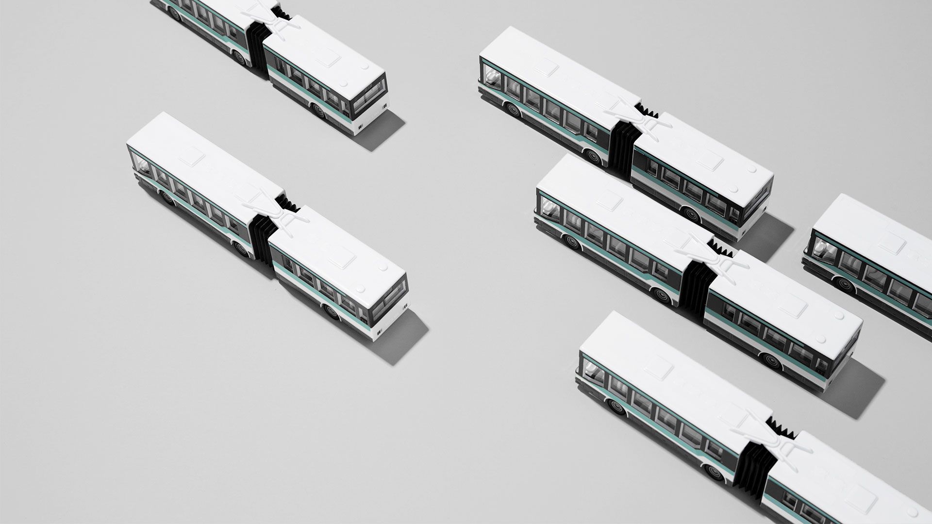 Sechs weiße Gelenkbusse mit schwarzen Verbindungsstücken, von oben auf grauem Untergrund angeordnet