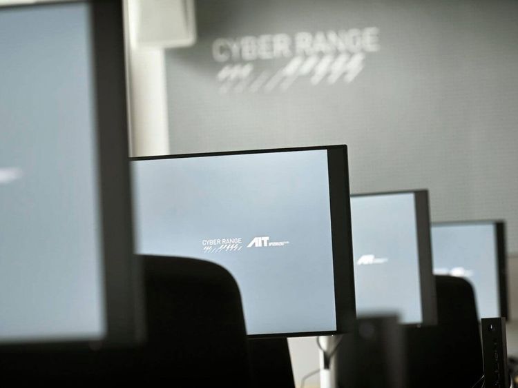 Mehrere Computerbildschirme in einem Raum mit der Aufschrift 'CYBER RANGE' an der Wand im Hintergrund