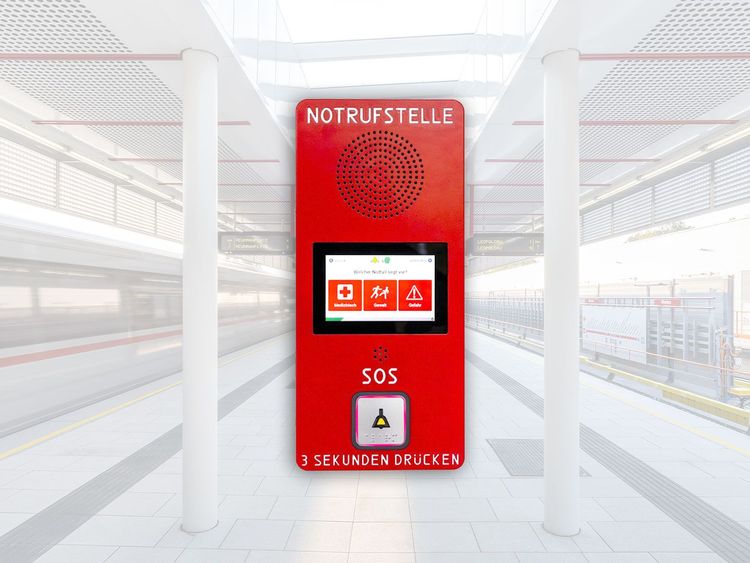 Rotes Notrufgerät mit Lautsprecher, Bildschirm und SOS-Knopf in einem hellen Bahnhofsgebäude