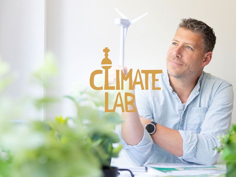 Mann mit hellblauem Hemd und Smartwatch blickt nachdenklich auf das Logo 'Climate Lab' mit Windkraftanlage im Hintergrund