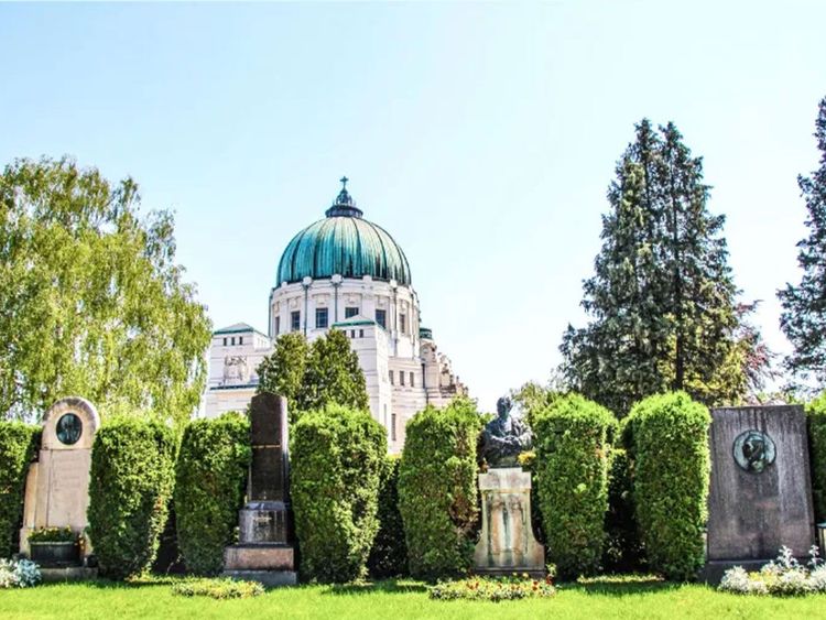 Historisches Mausoleum mit grünem Kuppeldach hinter einer Reihe von Grabsteinen und gepflegten Hecken