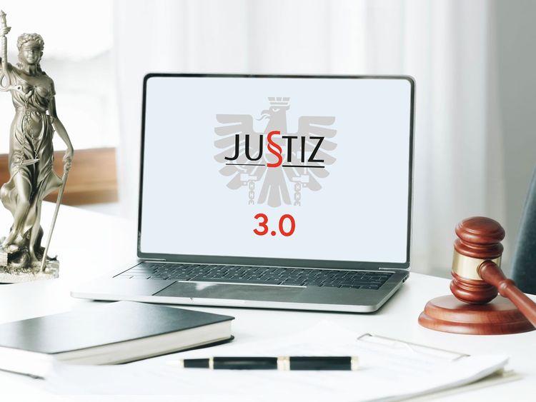 Laptop mit Justiz 3.0-Logo auf einem Schreibtisch, umgeben von Notizblock, Gerechtigkeitsfigur und Richterhammer.