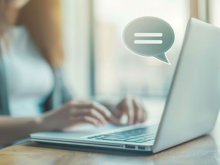 Person tippt auf Laptop-Tastatur mit Sprechblase über dem Bildschirm