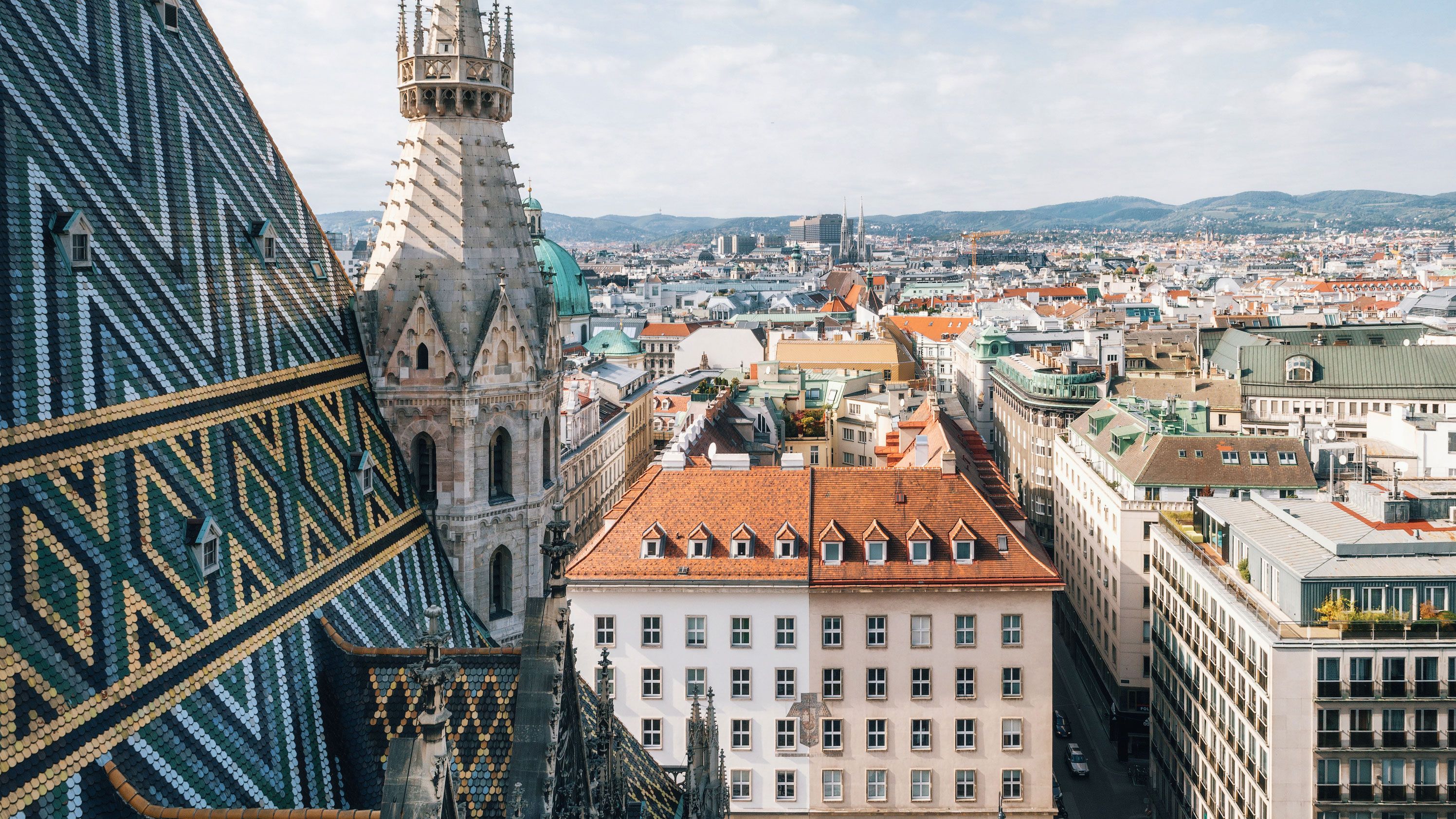 Blick auf das bunte Dach und den Turm des Stephansdoms in Wien sowie den Stephansplatz mit Menschen und umliegenden Gebäuden.